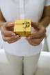Photo: Mature woman holding small gold gift box in hands, close-up, front view, mid-section Mature woman holding small gold gift box in hands, close-up, front view, mid-section