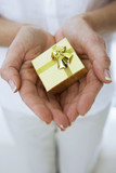 Photo: Mature woman holding small gold gift box in cupped hands, close-up, front view, mid-section Mature woman holding small gold gift box in cupped hands, close-up, front view, mid-section
