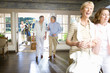 Photo: Two mature couples entering hotel foyer, man pushing luggage trolley through doorway in background, men talking golf, women smiling in foreground Two mature couples entering hotel foyer, man pushing luggage trolley through doorway in background, men talking golf, women smiling in foreground