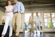 Photo: Two mature couples entering hotel foyer, smiling, man pushing luggage trolley through doorway in background (surface level) Two mature couples entering hotel foyer, smiling, man pushing luggage trolley through doorway in background (surface level)