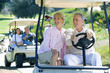 Photo: Two mature couples driving golf buggies along golf course pathway, focus on couple in foreground, smiling Two mature couples driving golf buggies along golf course pathway, focus on couple in foreground, smiling
