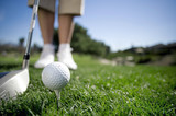 Photo: Mature woman preparing to tee off with driver on golf course, close-up, low section, focus on golf ball in foreground (surface level) Mature woman preparing to tee off with driver on golf course, close-up, low section, focus on golf ball in foreground (surface level)