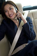 Photo: Businesswoman sitting in backseat of car, wearing seatbelt, using mobile phone, smiling, looking away Businesswoman sitting in backseat of car, wearing seatbelt, using mobile phone, smiling, looking away