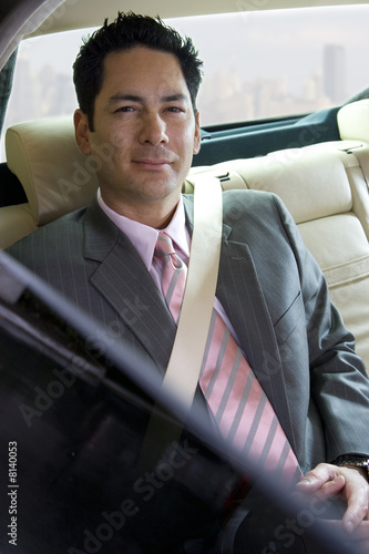 Businessman sitting in backseat of car, wearing seatbelt, view through open window, smiling, portrait Businessman sitting in backseat of car, wearing seatbelt, view through open window, smiling, portrait