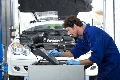 Computer Repair Stores on Car Mechanic In Blue Overalls Using Computer In Auto Repair Shop