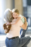 Photo: Grandmother and granddaughter (7-9) embracing in airport, senior woman crouching, girl holding soft toy, smiling Grandmother and granddaughter (7-9) embracing in airport, senior woman crouching, girl holding soft toy, smiling