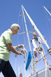 Photo: Two mature men preparing to set sail on yacht, one man untying mooring rope, smiling, low angle view Two mature men preparing to set sail on yacht, one man untying mooring rope, smiling, low angle view