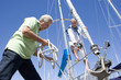 Photo: Two mature men preparing to set sail on yacht, one man untying mooring rope, smiling, low angle view Two mature men preparing to set sail on yacht, one man untying mooring rope, smiling, low angle view