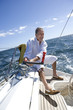Photo: Mature man sitting on deck of yacht out at sea, adjusting rigging using rope pulley, smiling (tilt) Mature man sitting on deck of yacht out at sea, adjusting rigging using rope pulley, smiling (tilt)