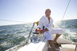 Photo: Mature man sitting on deck of yacht out at sea, turning rope pulley, smiling, portrait (tilt, backlit) Mature man sitting on deck of yacht out at sea, turning rope pulley, smiling, portrait (tilt, backlit)