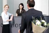 Photo: Businessman with bouquet of flowers being greeted by two women at office reception Businessman with bouquet of flowers being greeted by two women at office reception