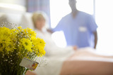 Photo: Male nurse by mature female patient in hospital bed, focus on bunch of flowers in foreground Male nurse by mature female patient in hospital bed, focus on bunch of flowers in foreground