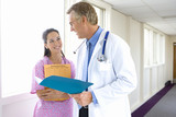Photo: Mature male doctor showing young female nurse folder in hospital corridor, smiling Mature male doctor showing young female nurse folder in hospital corridor, smiling
