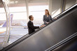 Photo: Businesswoman and businessman looking at each other on escalator in airport, smiling, side view Businesswoman and businessman looking at each other on escalator in airport, smiling, side view