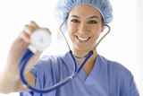 Photo: Young female nurse wearing hygiene cap, holding out stethoscope, smiling, portrait Young female nurse wearing hygiene cap, holding out stethoscope, smiling, portrait