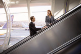 Photo: Businesswoman and businessman looking at each other on escalator in airport, smiling, side view Businesswoman and businessman looking at each other on escalator in airport, smiling, side view
