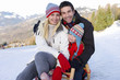 Photo: Young couple and daughter (6-8) embracing on sled in snow field, smiling, portrait, mountain range in background Young couple and daughter (6-8) embracing on sled in snow field, smiling, portrait, mountain range in background
