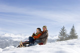 Photo: Boy and girl (7-9) riding sled on snow slope, smiling, portrait, wearing sunglasses, side view, mountain range in background Boy and girl (7-9) riding sled on snow slope, smiling, portrait, wearing sunglasses, side view, mountain range in background