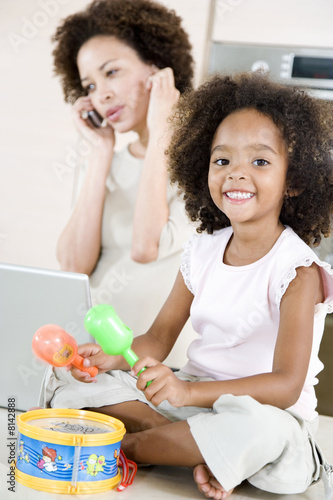 Photo: Little girl playing toy drum while mother tries to talk on the telephone Little girl playing toy drum while mother tries to talk on the telephone