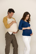 Photo: Young pregnant woman with hands on stomach, young man immitating woman with pillow Young pregnant woman with hands on stomach, young man immitating woman with pillow