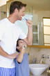 Father and son (6-8) brushing their teeth in bathroom, smiling