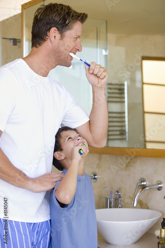 Photo: Father and son (6-8) brushing their teeth in bathroom, smiling Father and son (6-8) brushing their teeth in bathroom, smiling