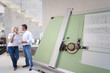 Photo: Couple smiling at each other indoors, blue prints on drafting board in foreground Couple smiling at each other indoors, blue prints on drafting board in foreground