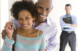 Photo: Couple holding house keys, smiling, portrait, male real estate agent standing in background Couple holding house keys, smiling, portrait, male real estate agent standing in background