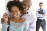 Photo: Couple holding house keys, smiling, portrait, male real estate agent standing in background Couple holding house keys, smiling, portrait, male real estate agent standing in background