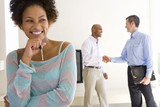 Photo: Woman holding house keys, smiling, male real estate agent and man shaking hands in background Woman holding house keys, smiling, male real estate agent and man shaking hands in background