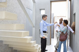 Photo: Male real estate agent handing keys to couple, standing by stairs, smiling, side view Male real estate agent handing keys to couple, standing by stairs, smiling, side view