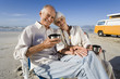 Photo: Senior couple on beach by camper van drinking from insulated flask, smiling, portrait Senior couple on beach by camper van drinking from insulated flask, smiling, portrait