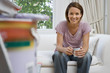 Photo: Young woman sitting on sofa with mug, paint pot and brush on ladder in foreground, smiling, portrait (differential focus) Young woman sitting on sofa with mug, paint pot and brush on ladder in foreground, smiling, portrait (differential focus)