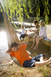 Photo: Boy (6-8) in hammock by family fishing from jetty in background, elevated view (lens flare) Boy (6-8) in hammock by family fishing from jetty in background, elevated view (lens flare)