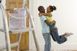 Young couple embracing by paint pot on ladder, man lifting woman off ground, side view