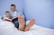 Photo: Father reading to son (4-6) in bed, close-up of father's feet (differential focus) Father reading to son (4-6) in bed, close-up of father's feet (differential focus)
