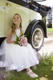 Photo: Flower girl (10-12) with bouquet of flowers by vintage car, smiling, low angle view Flower girl (10-12) with bouquet of flowers by vintage car, smiling, low angle view