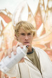 Photo: Portrait of a young man holding a spray can in front of a wall covered in graffiti Portrait of a young man holding a spray can in front of a wall covered in graffiti