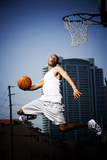 Foto: Young African American man jumping with a basketball on an urban basketball court Young African American man jumping with a basketball on an urban basketball court