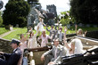 Photo: Wedding party throwing confetti on bride and groom in convertible vintage car by church, smiling Wedding party throwing confetti on bride and groom in convertible vintage car by church, smiling