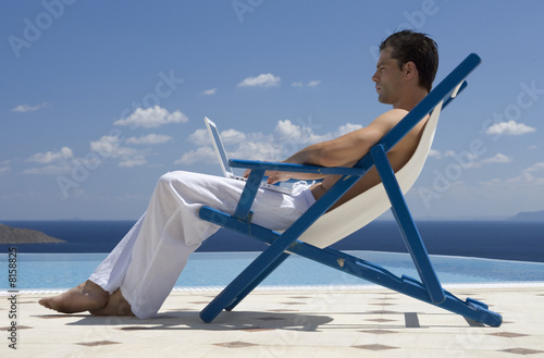 Photo: A man sitting on a deck chair using a laptop A man sitting on a deck chair using a laptop