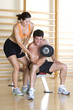 Woman feeling biceps of bare chested man lifting weights in gym, smiling