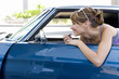 Photo: Young woman leaning on open door of car applying lipstick in rear view mirror, side view Young woman leaning on open door of car applying lipstick in rear view mirror, side view