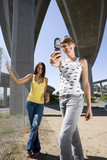 Photo: Young woman by friend, taking photograph beneath overpasses, smiling, portrait, low angle view Young woman by friend, taking photograph beneath overpasses, smiling, portrait, low angle view