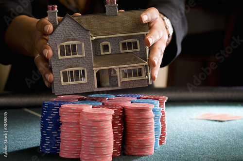 Photo: Woman placing model house on pile of gambling chips on table, mid section Woman placing model house on pile of gambling chips on table, mid section