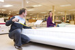 Man measuring bed in furniture shop, family in background