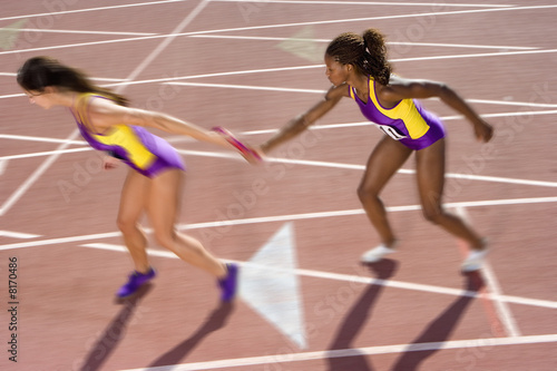 Photo: Female relay athletes passing baton (blurred motion) Female relay athletes passing baton (blurred motion)