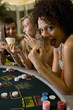 Young woman gambling at poker table in casino, showing cards, smiling, portrait
