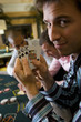 Young man gambling at poker table in casino, showing cards, smiling, portrait