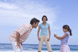 Parents smiling at daughter (6-8) with camcorder on beach, low angle view
